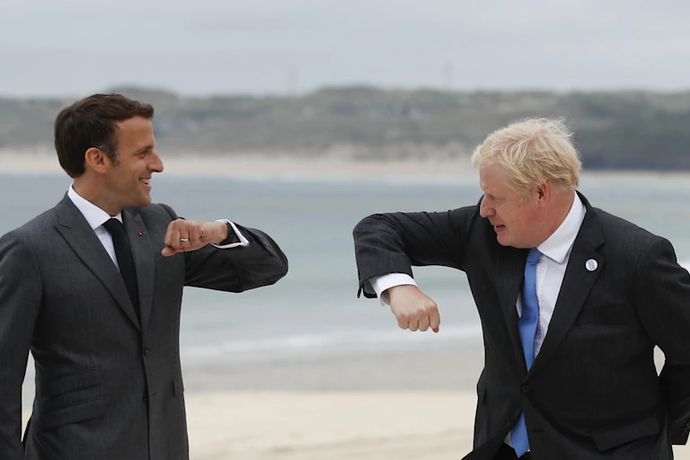 French President Emmanuel Macron and British Prime Minister Boris Johnson hold out their arms with their elbows pointing toward each other as they prepare for an elbow bump during a G-7 meeting