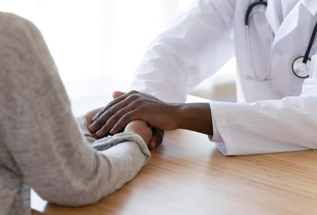 A doctor's hands clasping a patient's hands.