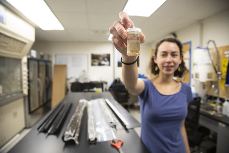 A female scientist holds a small container with tiny flecks of charcoal in it.