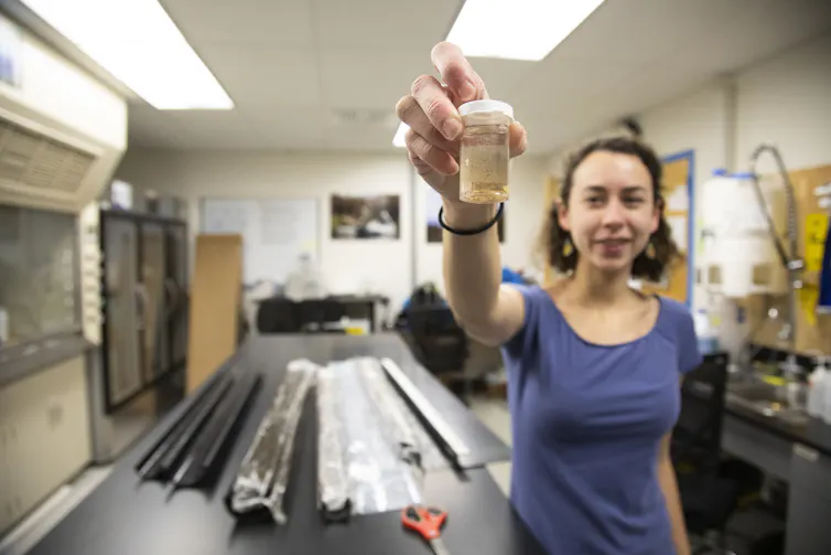 A female scientist holds a small container with tiny flecks of charcoal in it.