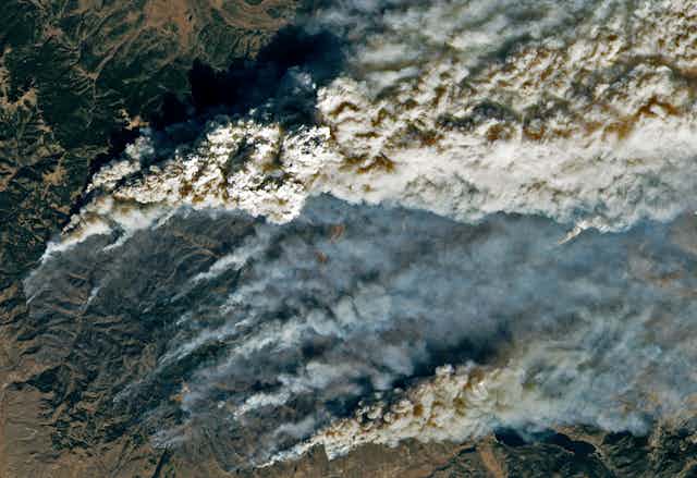 A satellite image shows smoke trailing up from multiple hotspots on the fire line in the mountains.