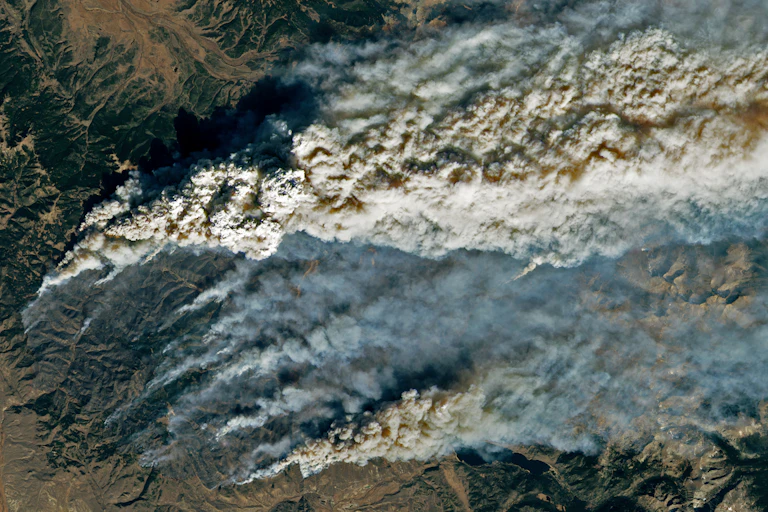 A satellite image shows smoke trailing up from multiple hotspots on the fire line in the mountains.