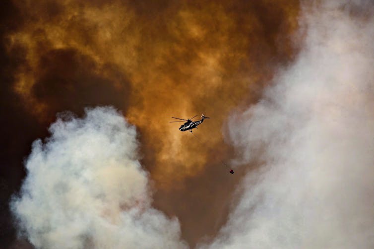 A helicopter is seen in the smoke of a wildfire.