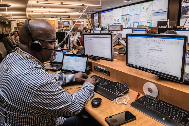 A man with headphones on with three computer screens in front of him.