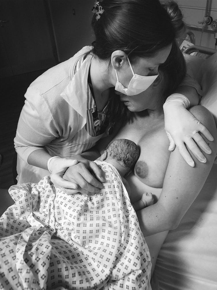 Midwife reassuring woman holding a newborn baby in hospital