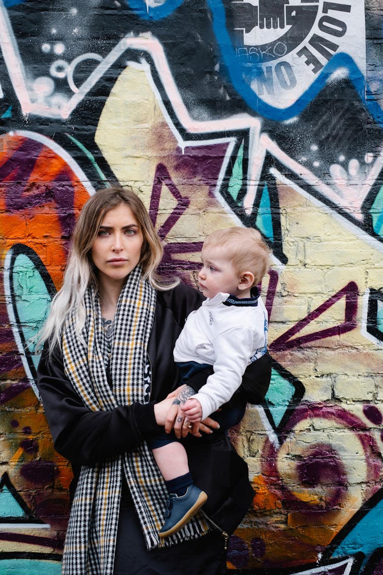 Woman holding her son and standing in front of graffiti