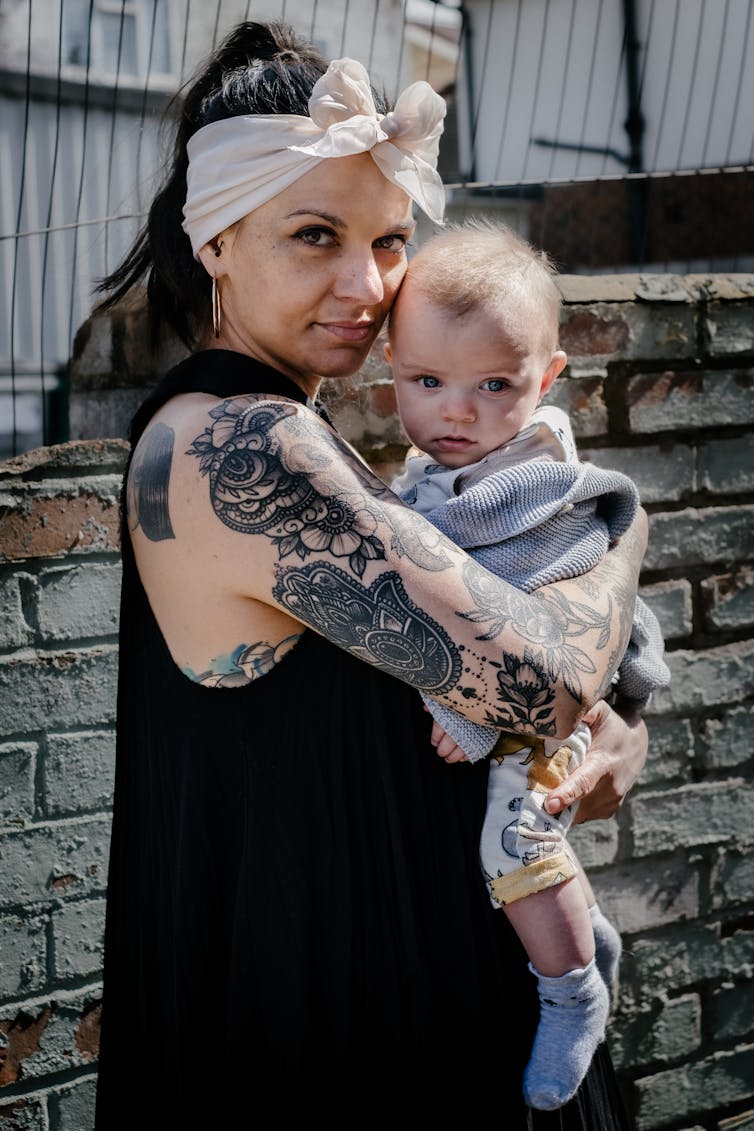 Woman with tattoos wearing a headscarf and holding a baby