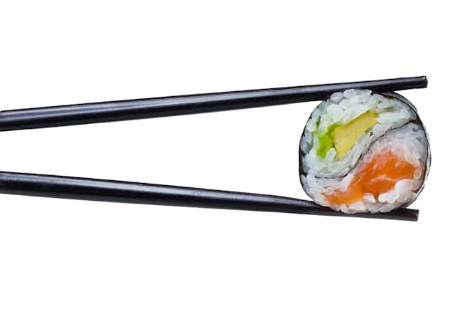 Pieza de sushi entre dos palillos negros.