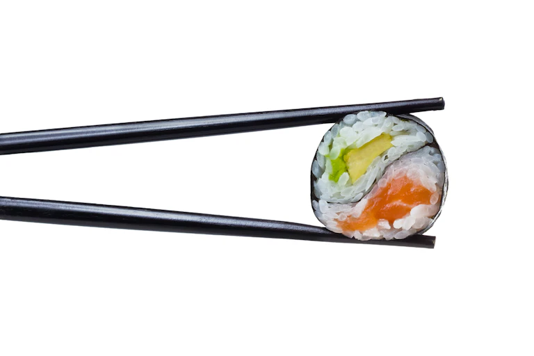 Pieza de sushi entre dos palillos negros.