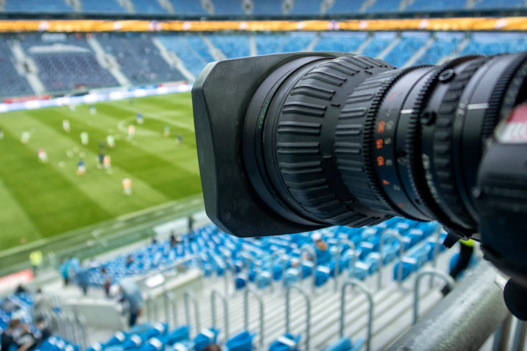Cámara de tv con partido de fútbol de fondo.