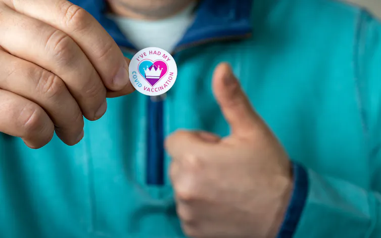 A man showing a sticker that says 'I've had my COVID vaccination'