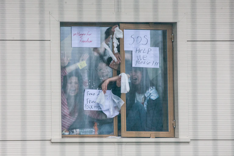 Detainees in Yarl's Wood Immigration Removal Centre hold up signs calling for help reading 'hunger for freedom', 'SOS' and 'help we please'