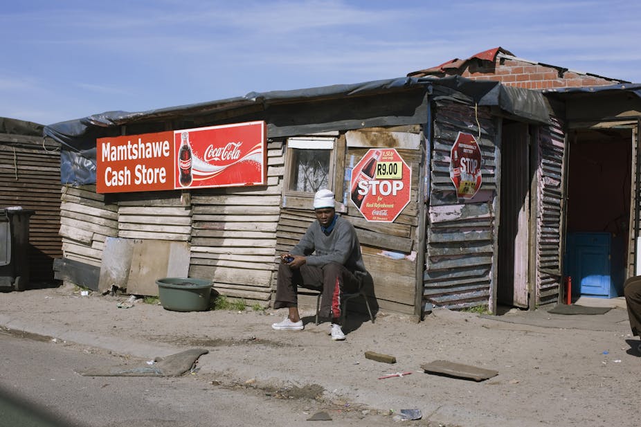A young man sits outside an informally built structure with commercial signage