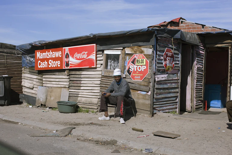 A young man sits outside an informally built structure with commercial signage
