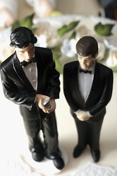 Statuettes of two men in tuxedos adorn the top of a wedding cake.