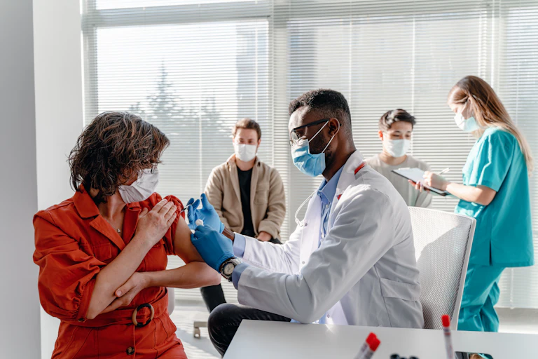 Person getting vaccinated in a clinic with two other people getting checked in.