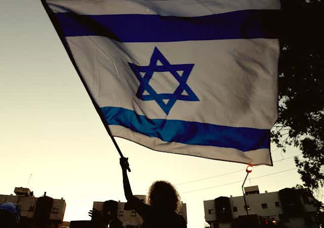 Woman waves an Israeli flag at dusk