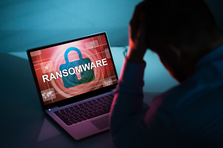 shadow of a man with his head in his hands looking at a laptop screen that says RANSOMWARE