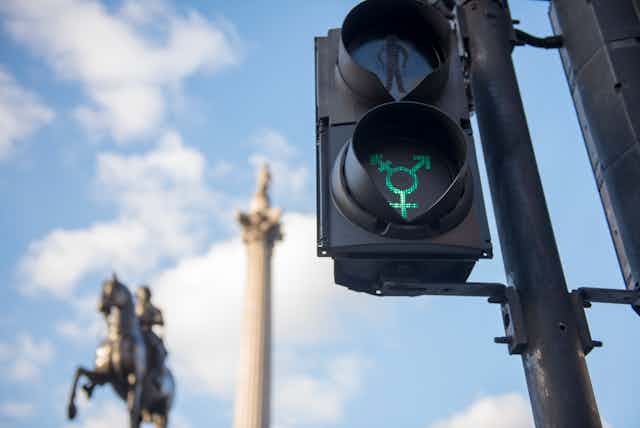 A traffic light altered so the green light flashes the symbol of gender diversity.