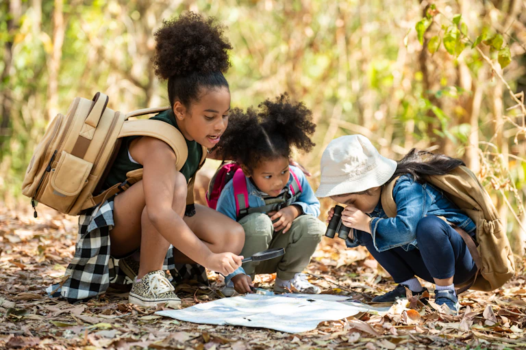 Three girls look at a map in the middle of a forest.