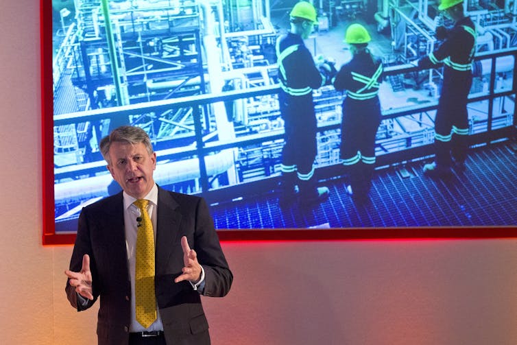 Shell's CEO speaking in front of a photo of fossil fuel workers