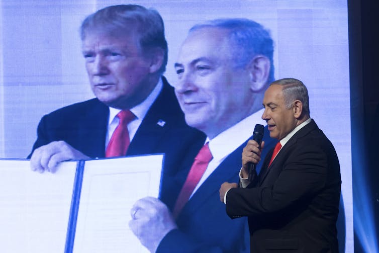 Benjamin Netanyahu se para frente a una gran foto que lo muestra a él y al presidente de Estados Unidos, Donald Trump.