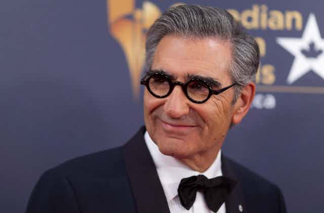 A man in round glasses and a black bowtie smiling.