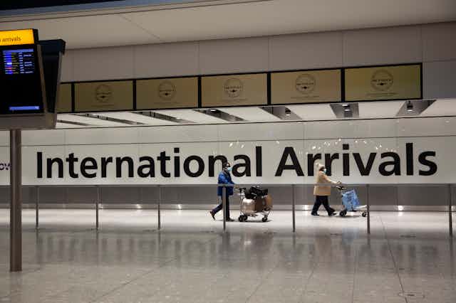 Two people walking through airport in front of sign saying 'international arrivals'
