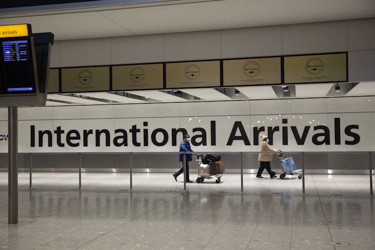 Two people walking through airport in front of sign saying 'international arrivals'
