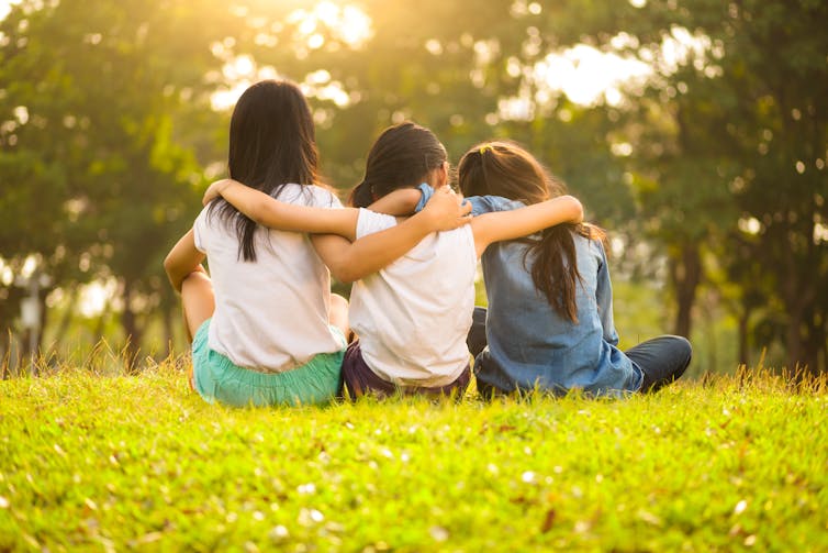Three girls sitting in a park with their arms around each other.