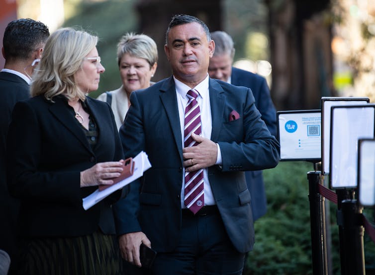 John Barilaro smooths his tie while walking out in public.