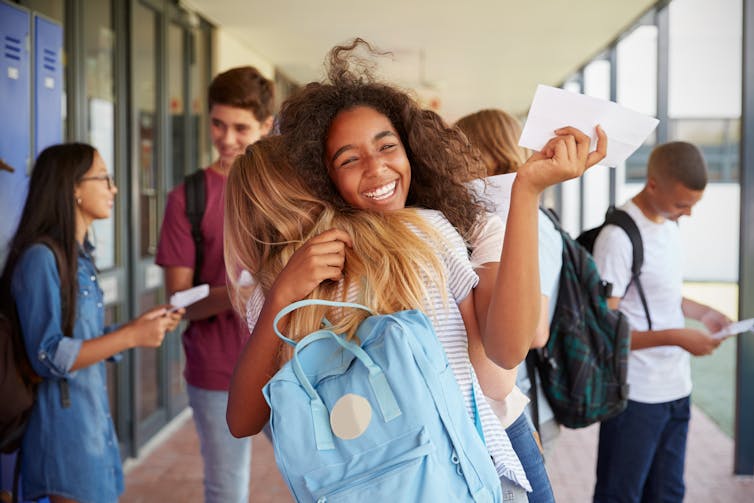 Girl hugging her schoolfriend and holding letter in her hand.