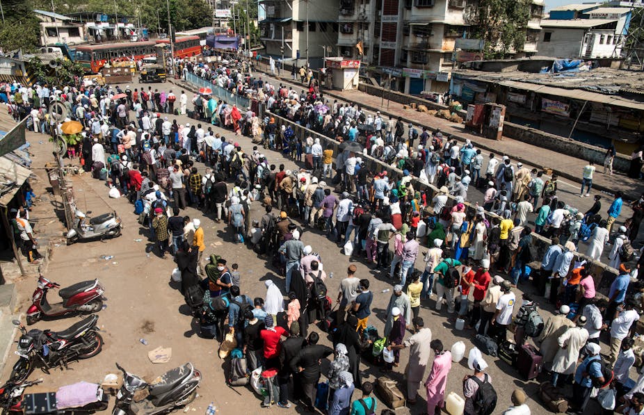 Migrant workers with their family stand in queue to board a bus to take them to railway terminus for boarding a special train back home during a nationwide lockdown
