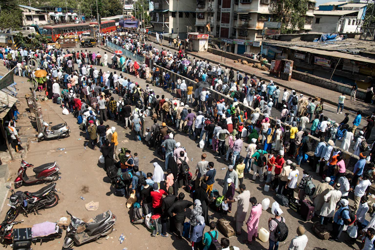 Migrant workers with their family stand in queue to board a bus to take them to railway terminus for boarding a special train back home during a nationwide lockdown
