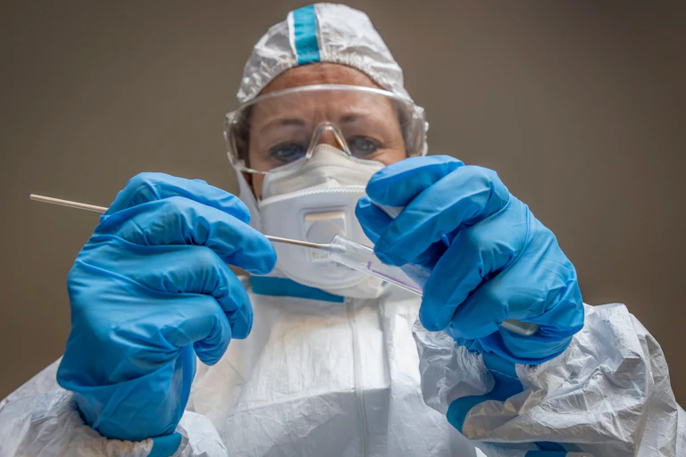 Medic in PPE holding a swab test.