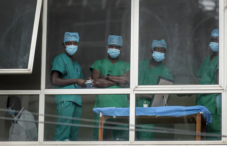 Medical staff wearing masks look out of a hospital window.
