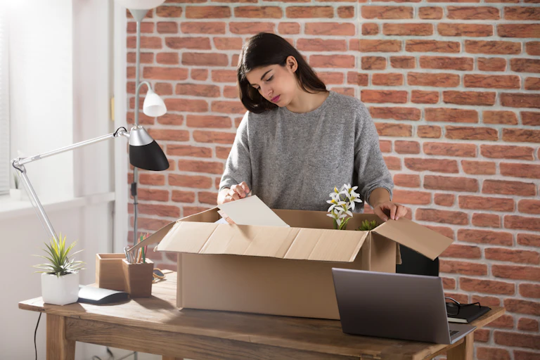 A woman stands at a desk putting her personal items in a box.