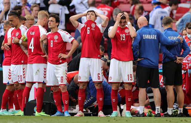 Members of the Danish football team looking visibly distressed as they stand around their collapsed teammate, receiving medical attention.
