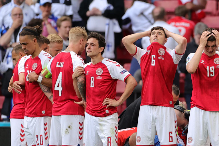 Members of the Danish football team looking visibly distressed as they stand around their collapsed teammate, receiving medical attention.