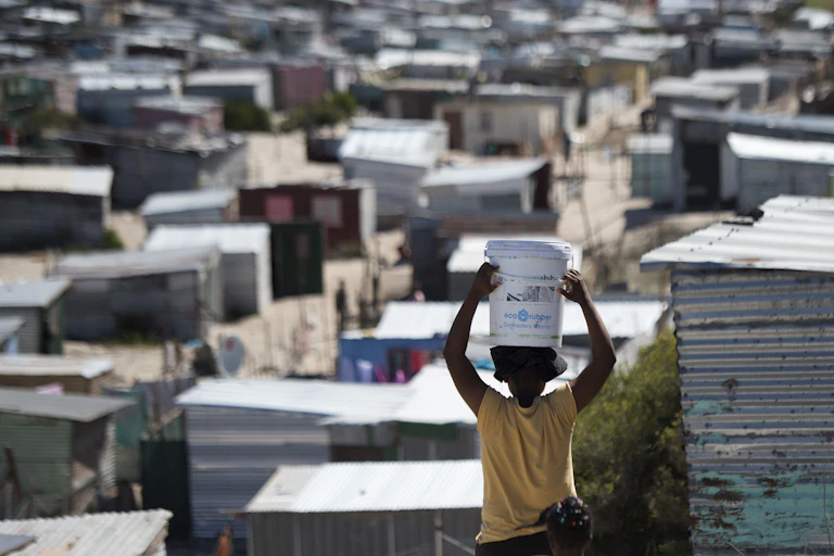 A woman carries a bucket of fresh water to an informal settlement