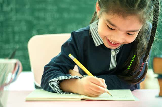 A girl holds a pencil at a desk.