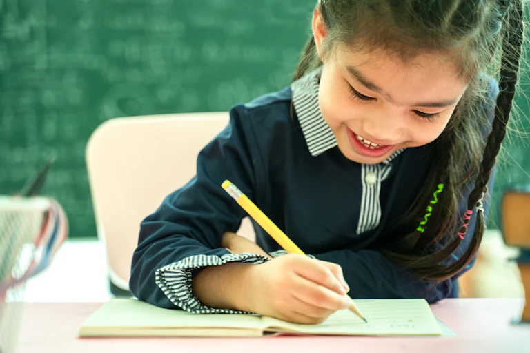 A girl holds a pencil at a desk.