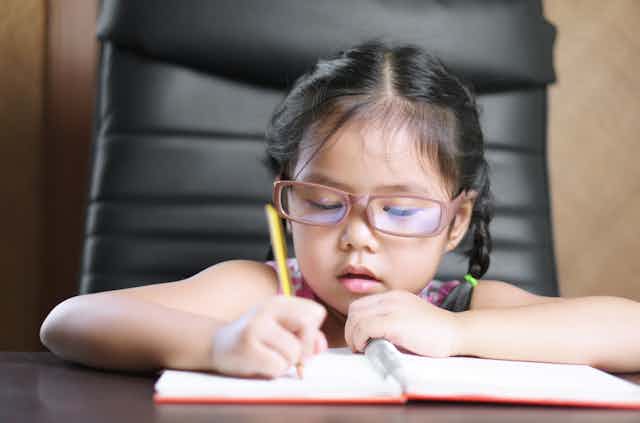 Young girl wearing glasses writes in a notebook.