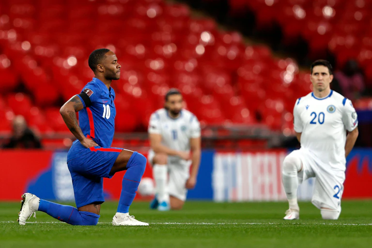 Raheem Stirling takes a knee on the football pitch next to two other football kneeling players