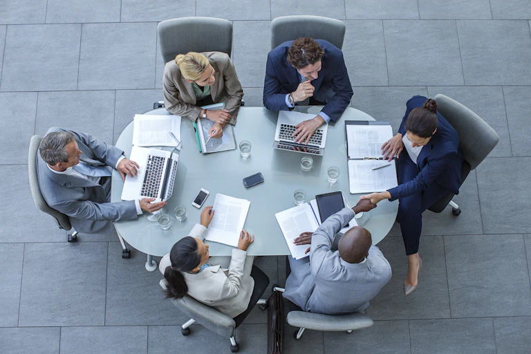 High angle view of people in business attire shaking hands at a conference table in an office.