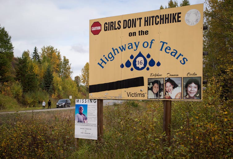 A road sign depicting three missing Indigenous women, reading 'Girls don't hitchhike on the Highway of Tears'