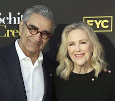 A man in glasses in white shirt and jacket and a woman in black dress stand next to each other smiling.