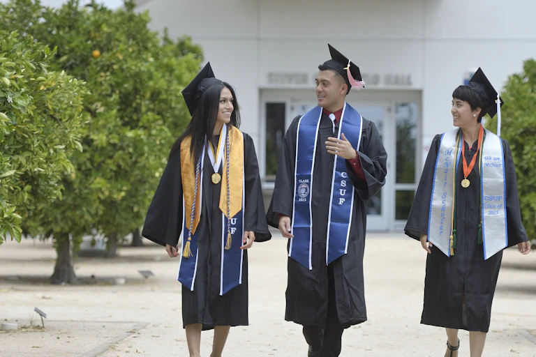Three college grads speak to one another in their caps and gowns.