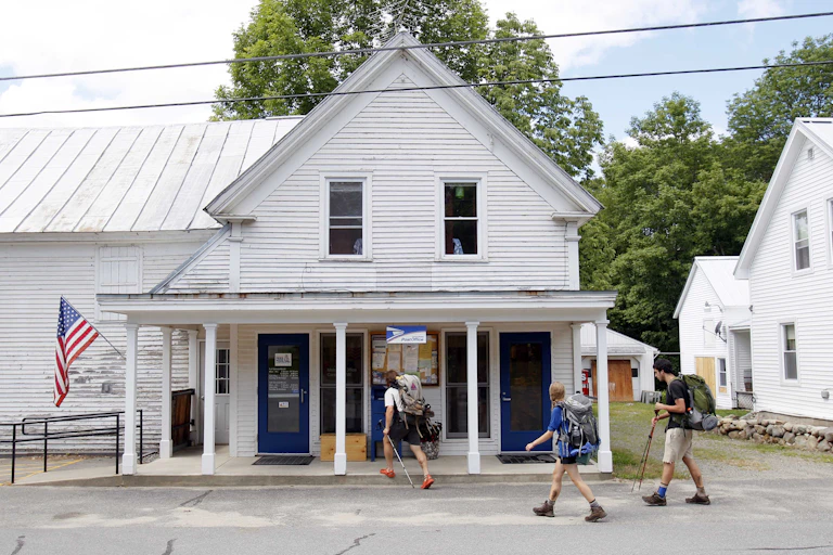Hikers walk past a white building housing a U.S. post office near the Appalachian trail in maine