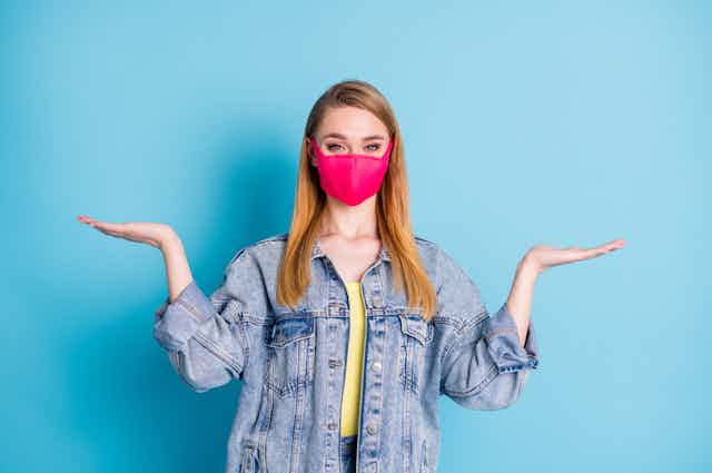 Young woman wearing mask with hands in air, undecided